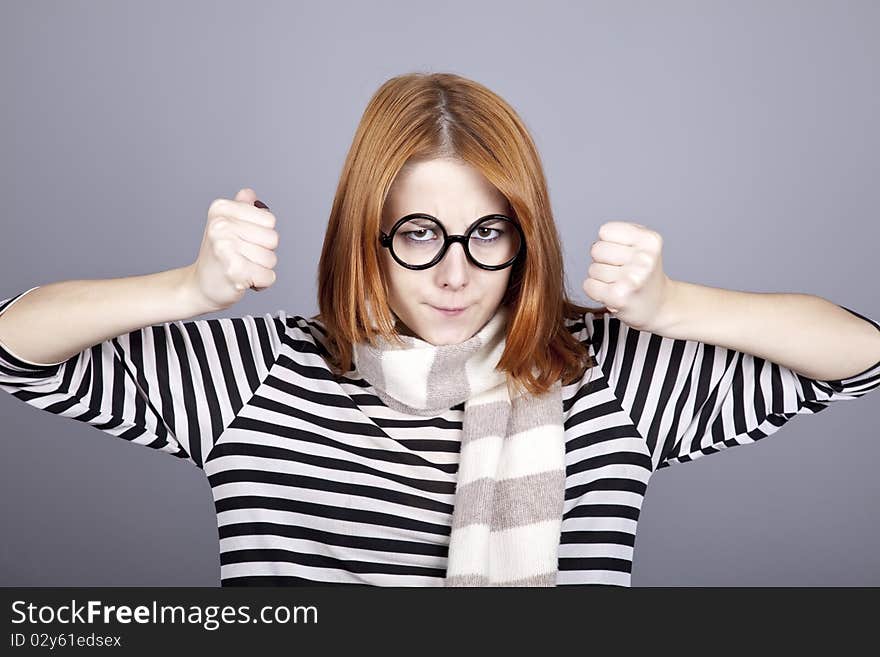 Angry red-haired girl in glasses and scarf. Studio shot.