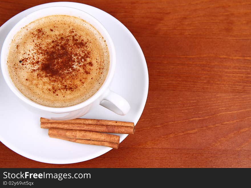 Cup of coffee sprinkled with cinnamon and with cinnamon sticks on wooden background. Cup of coffee sprinkled with cinnamon and with cinnamon sticks on wooden background