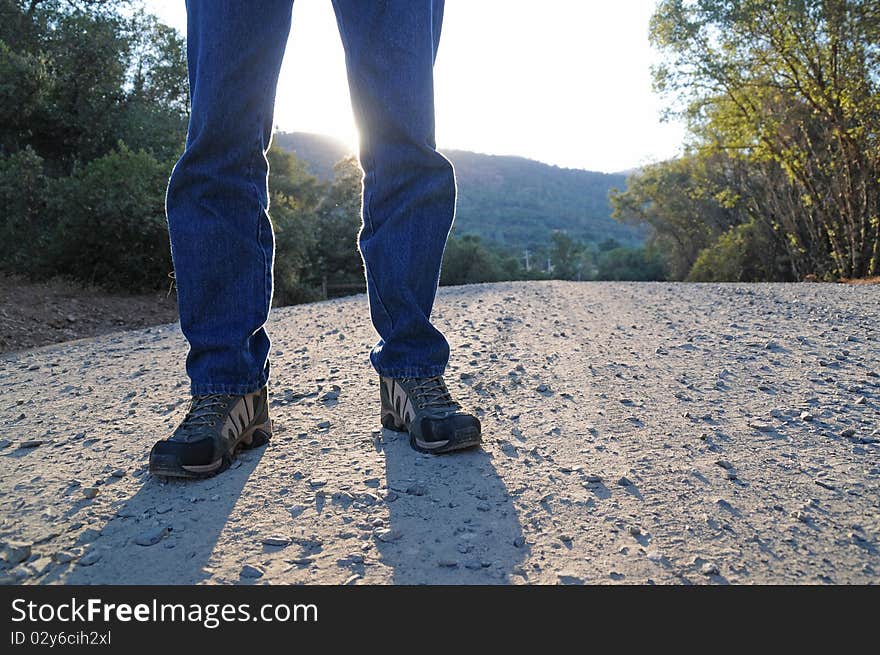 A man standing on a gravel road with his shadow in front of him