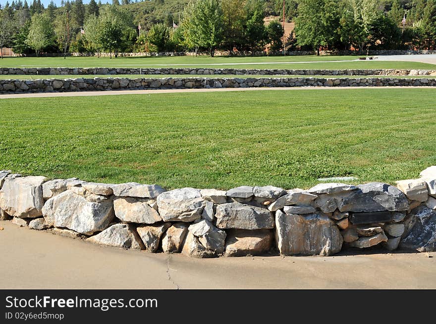 A modern amphitheater with grass and a rock wall during the day.