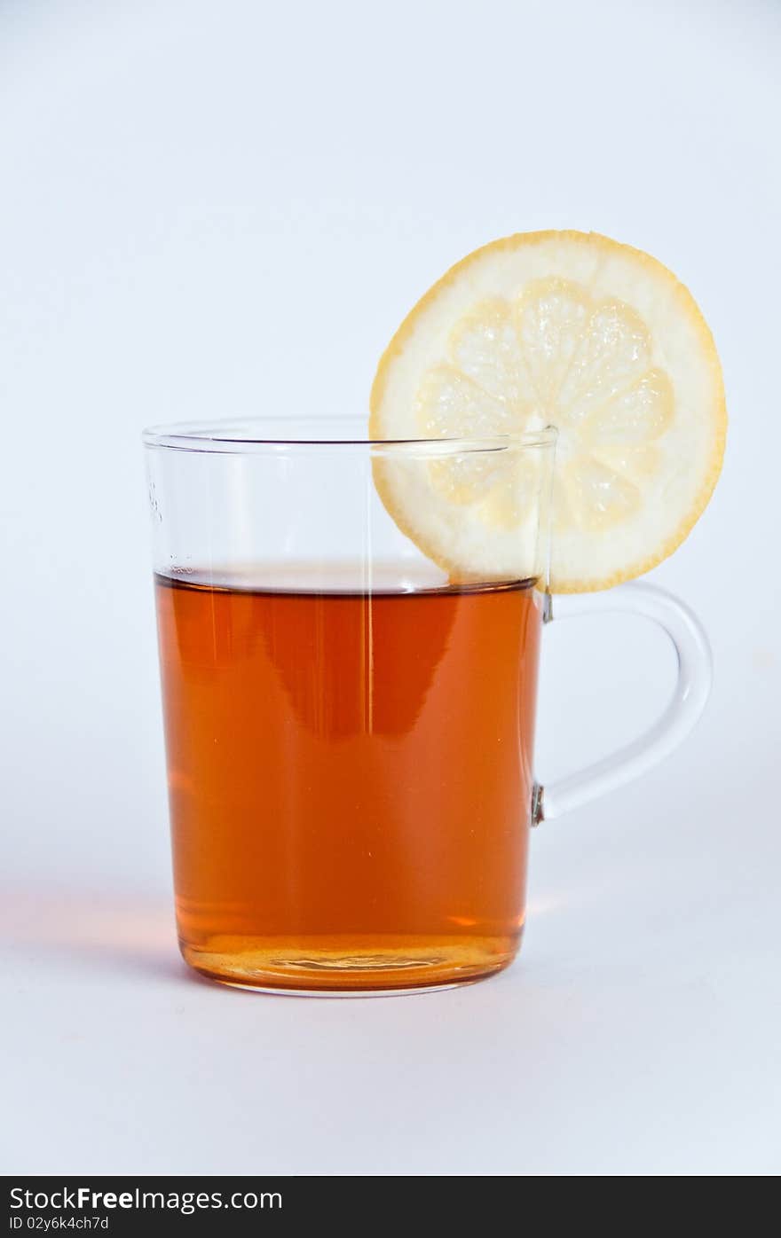 Glass of hot black tea with lemon and a tea pot