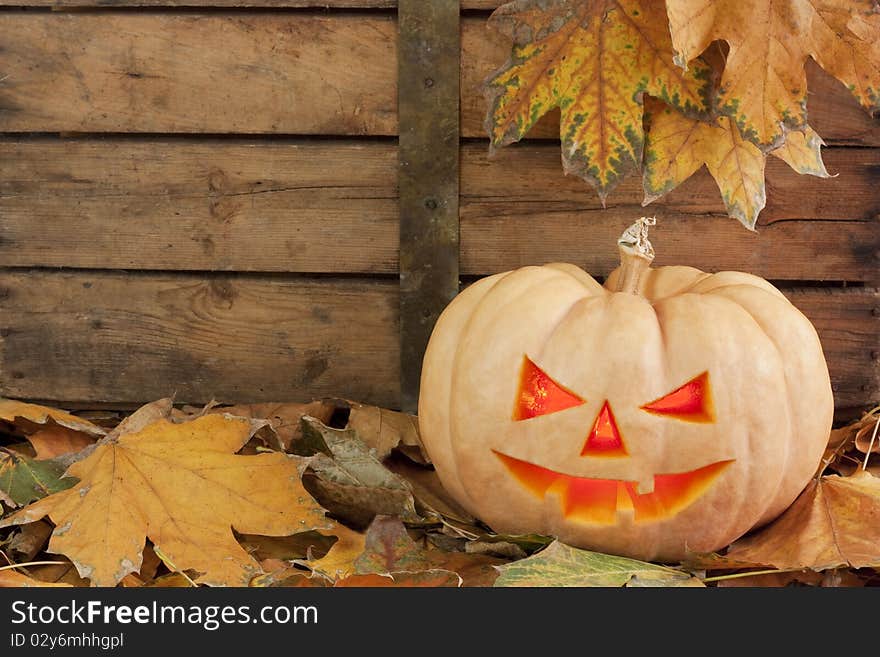 Creepy carved pumpkin face on wooden bacground and autumn leafs. Creepy carved pumpkin face on wooden bacground and autumn leafs