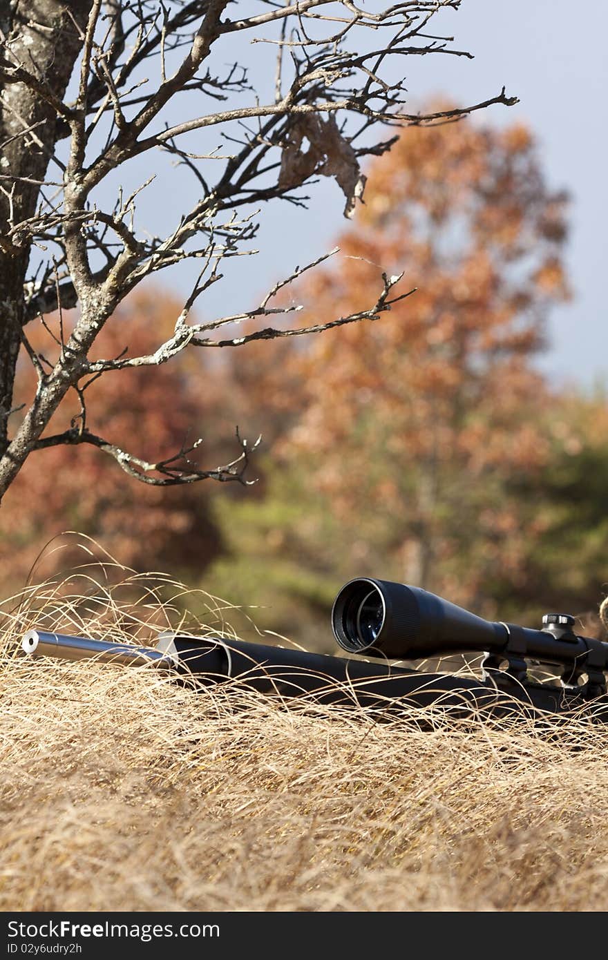 Sniper laying on the ground covered in a ghille suite tall grass and trees in the background