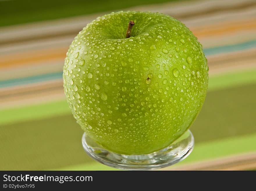 Single green apple on the glass plate covered with dropletes of water. Single green apple on the glass plate covered with dropletes of water