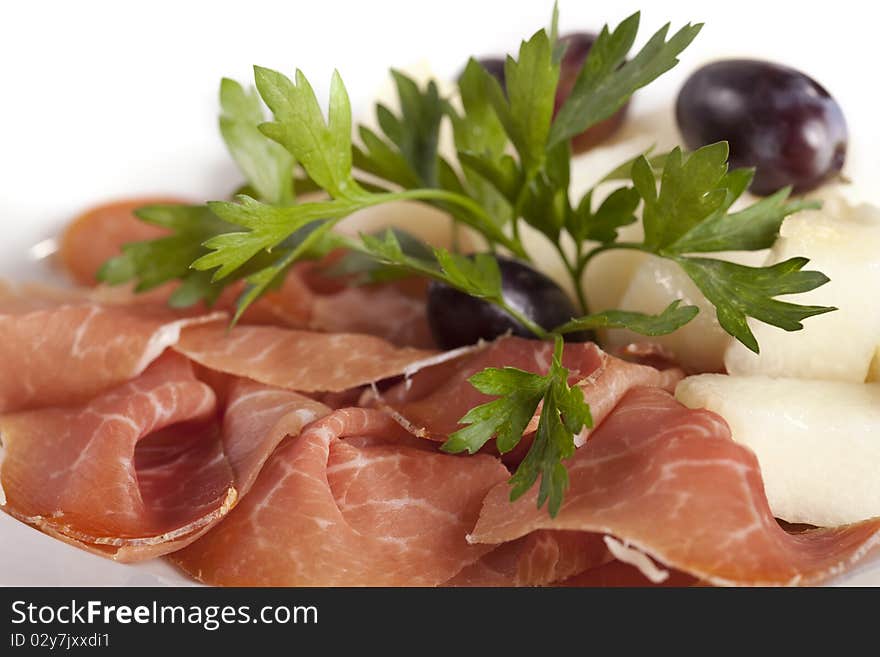 Smoked meat beef slices with melon cubes and grapes on ceramic plate