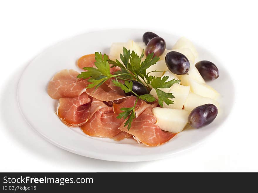 Smoked meat beef slices with melon cubes and grapes on ceramic plate