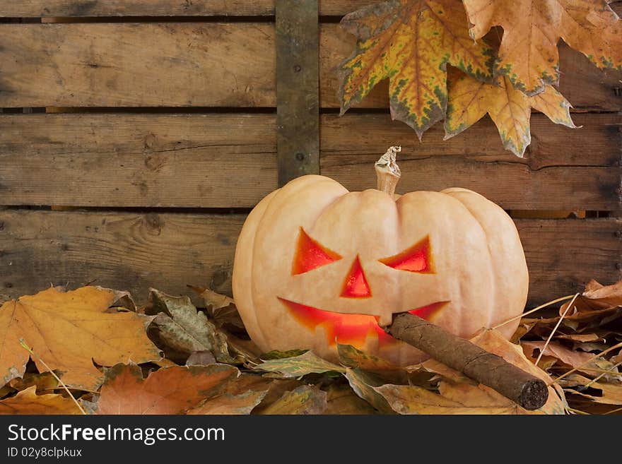 Creepy carved pumpkin face smoking a cigar on wooden bacground and autumn leafs. Creepy carved pumpkin face smoking a cigar on wooden bacground and autumn leafs