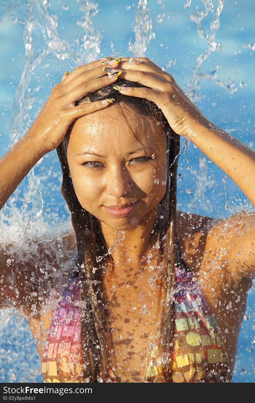 Beautiful woman bathes in pool under water splashes