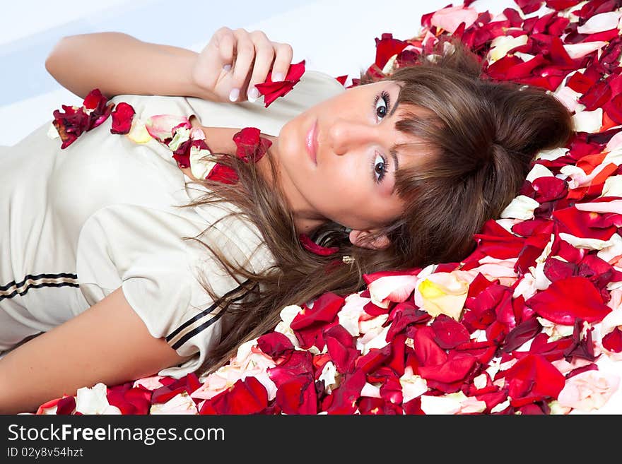 A young woman lying on the studio floor with red rose petals. A young woman lying on the studio floor with red rose petals