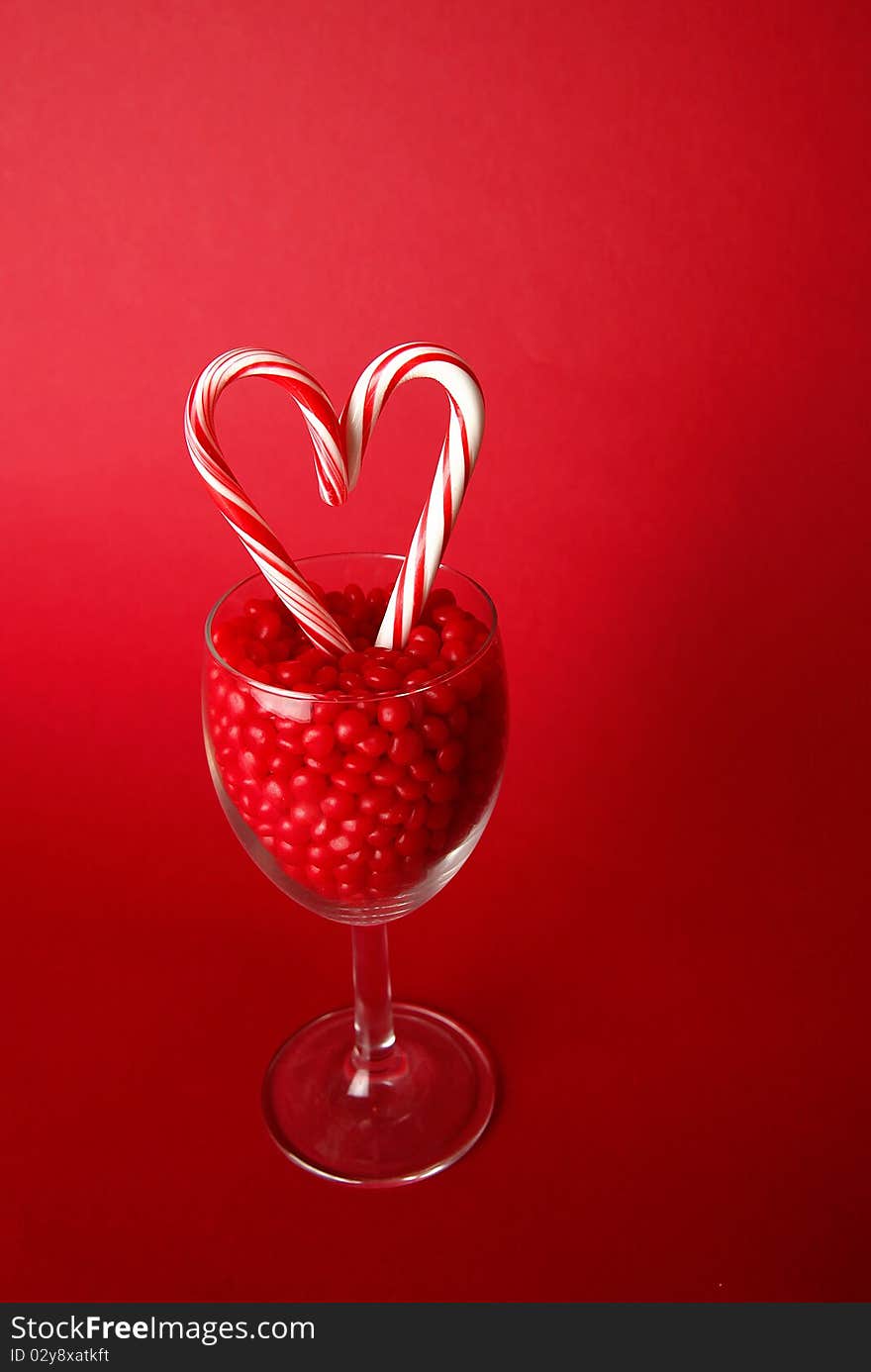 Heart made out of candy canes in a goblet filled with red hot candies on a red background. Heart made out of candy canes in a goblet filled with red hot candies on a red background