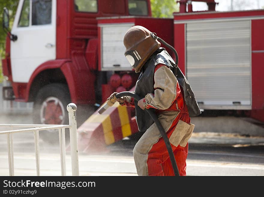 Worker in a protective suit spraying sand  with abrasive peeler