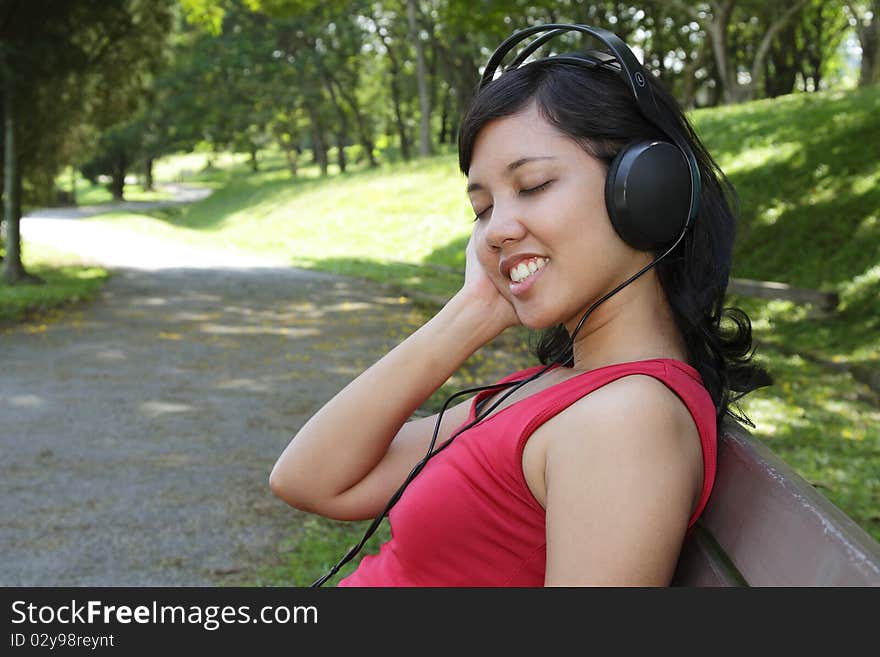 An Asian woman listening to music at a park