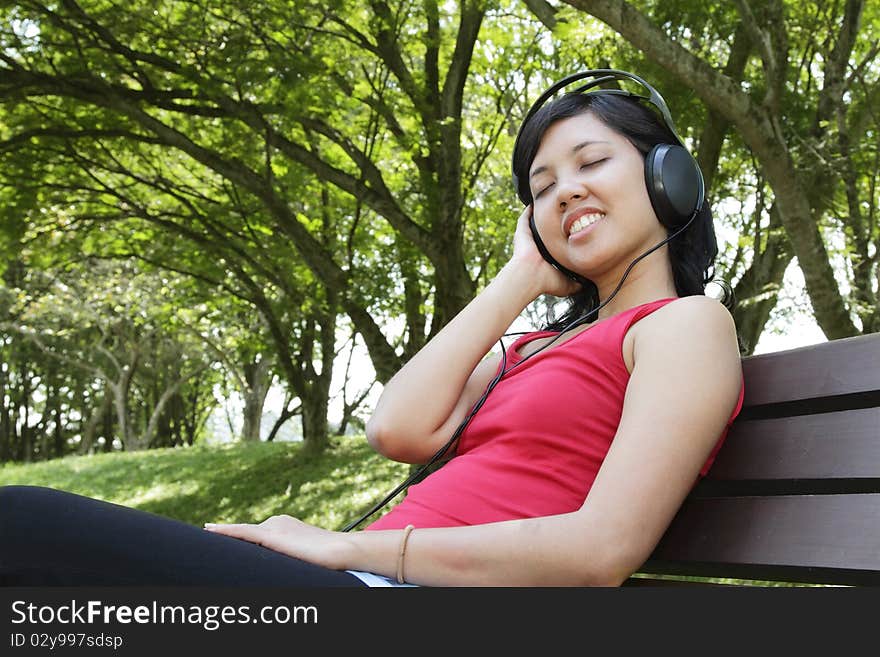 An Asian woman listening to music at a park