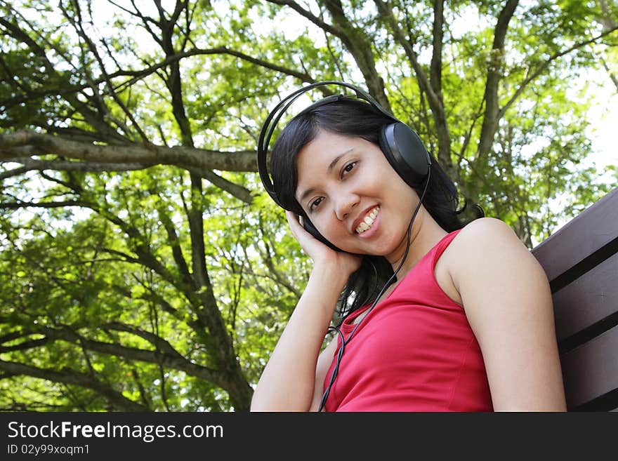 An Asian woman listening to music at a park