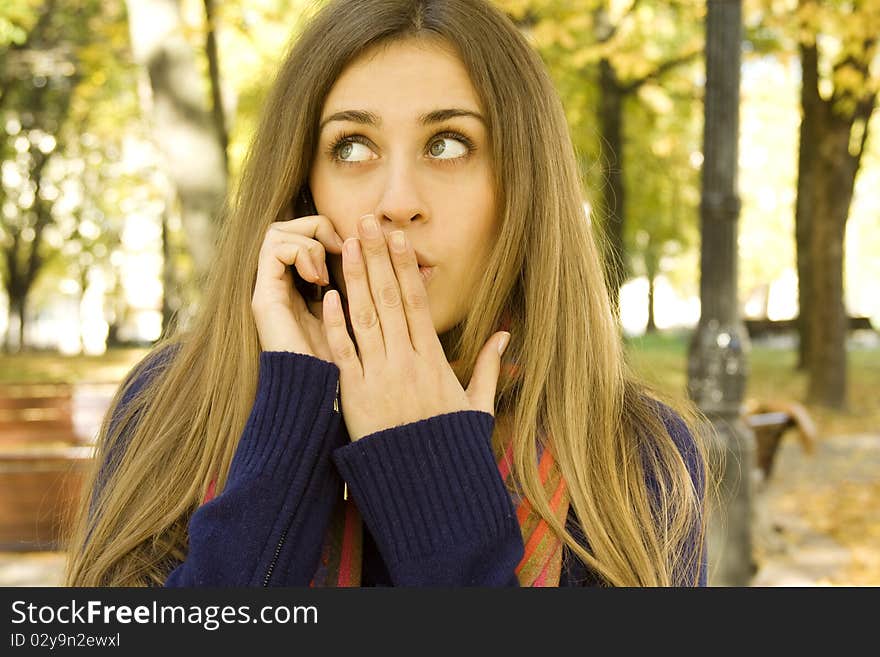 Autumn portrait of a beautiful girl outside on the phone shocking news. Autumn portrait of a beautiful girl outside on the phone shocking news