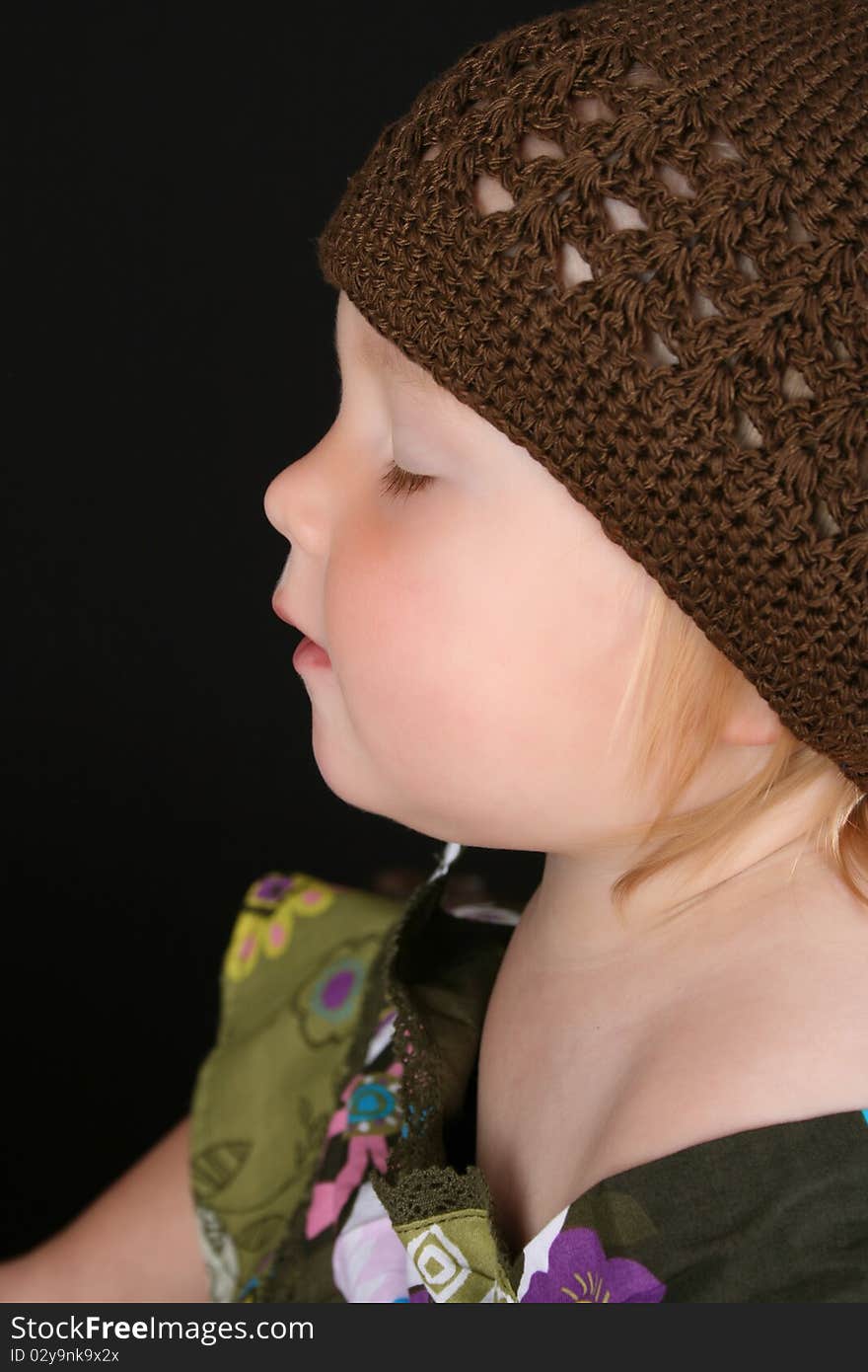 Cute little girl wearing a brown knitted hat sitting with eyes closed. Cute little girl wearing a brown knitted hat sitting with eyes closed