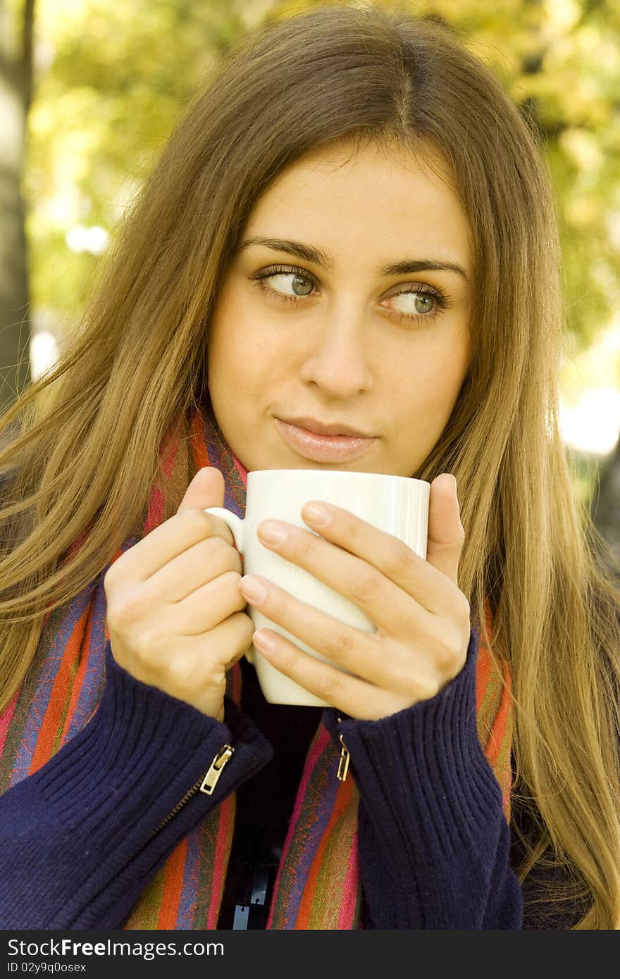 Autumn portrait of an attractive young woman wearing a soft sweater and scarf, holding a cup coffee (or tea). Autumn portrait of an attractive young woman wearing a soft sweater and scarf, holding a cup coffee (or tea)