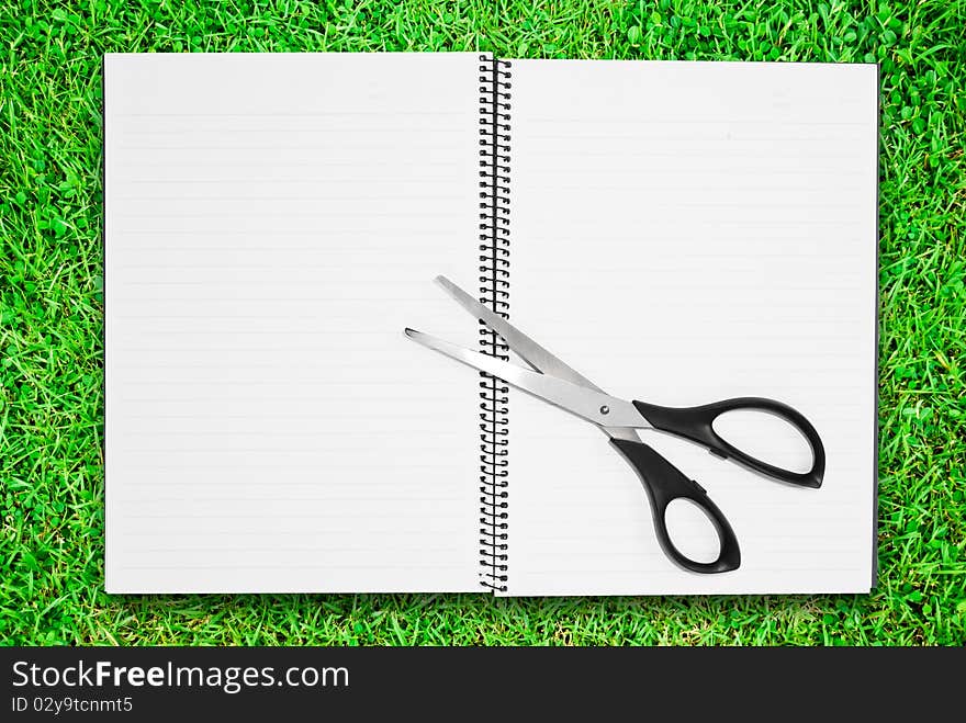 Blank notebook open two page with scisscors on green grass field. Blank notebook open two page with scisscors on green grass field