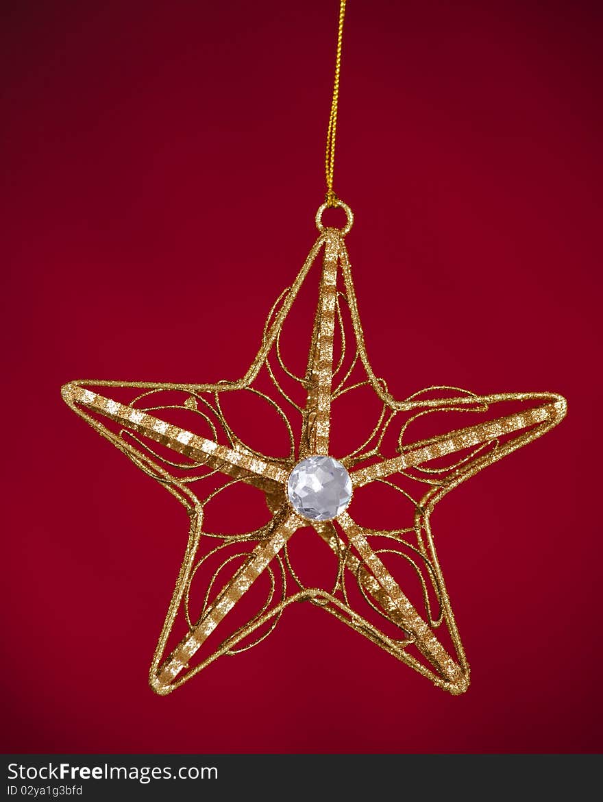 A gold Christmas tree star ornament isolated against a red background. A gold Christmas tree star ornament isolated against a red background.