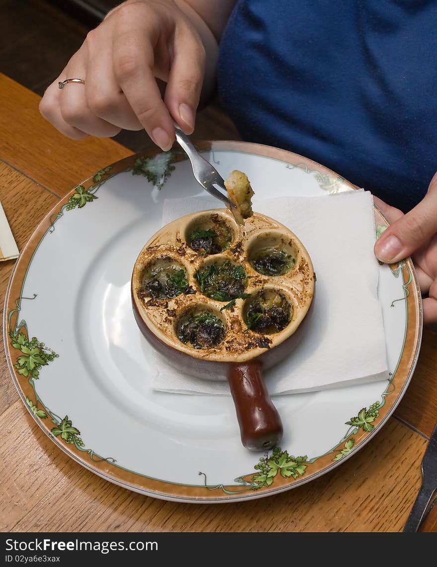 Plate with baked snail, piece of bread with a fork, dip it in the oil