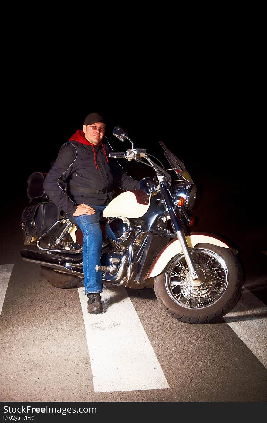 Lonely rider sitting on custom motorcycle in the middle of night street.