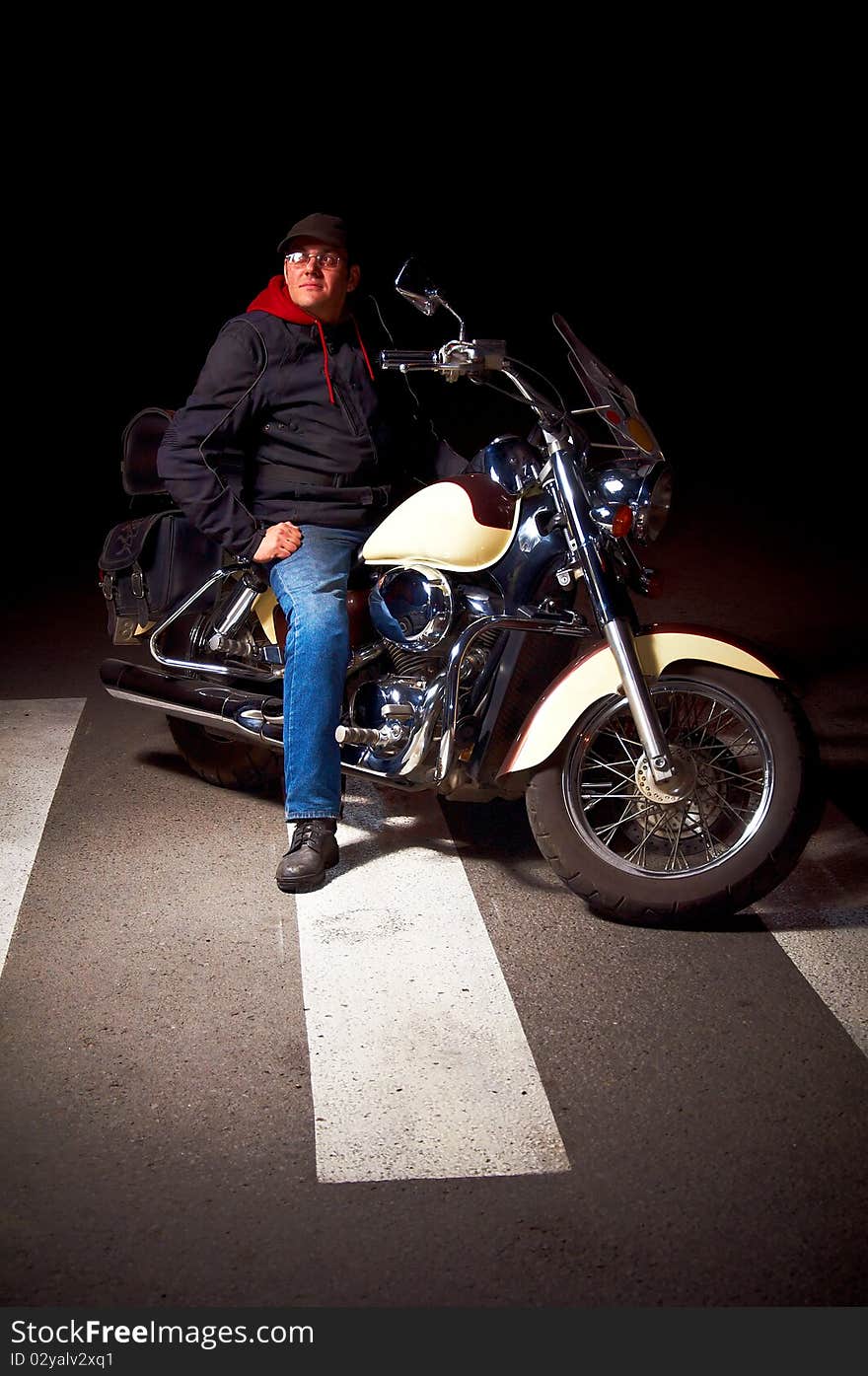 Lonely rider sitting on custom motorcycle in the middle of night street.