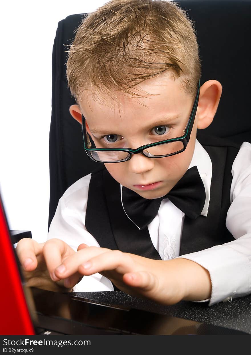 Child in white shirt and bow tie looks in laptop. Child in white shirt and bow tie looks in laptop