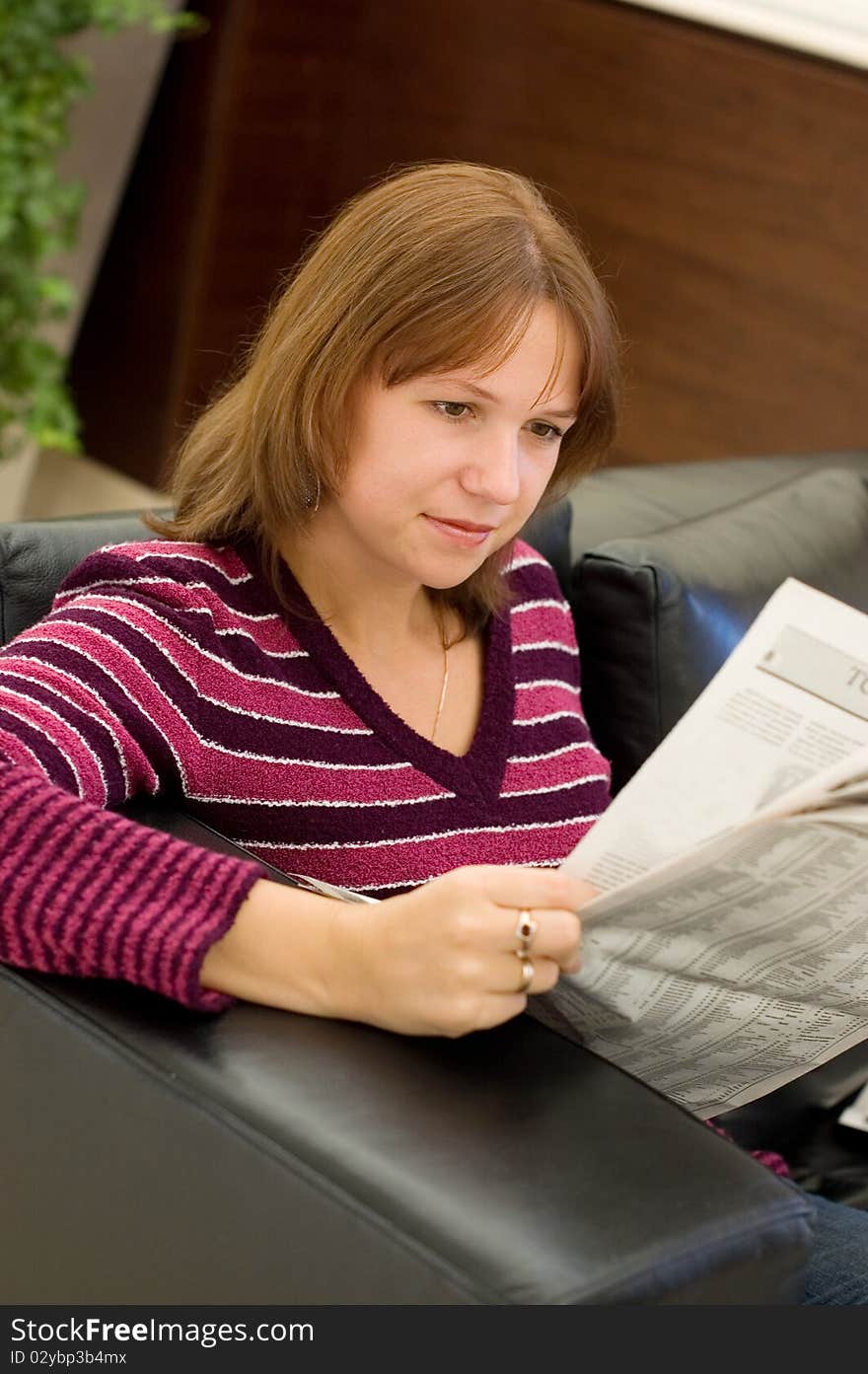 The girl reads the newspaper in an armchair at office