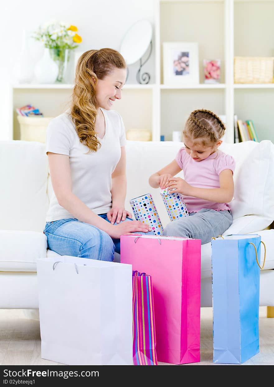 Mother looking at her little daughter openning gift - at home. Mother looking at her little daughter openning gift - at home