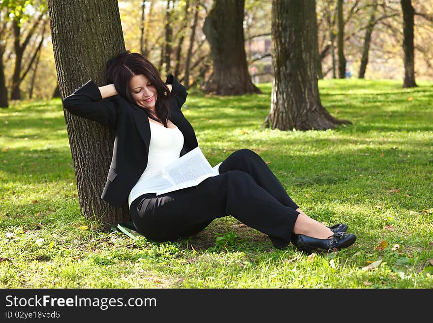 Young businesswoman sitting on the grass and reading book outdoor. Young businesswoman sitting on the grass and reading book outdoor