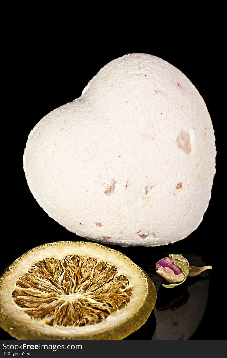 Bath salts in the form of the heart with a dry flowers and the dried slices of lemon on a black background. Bath salts in the form of the heart with a dry flowers and the dried slices of lemon on a black background.