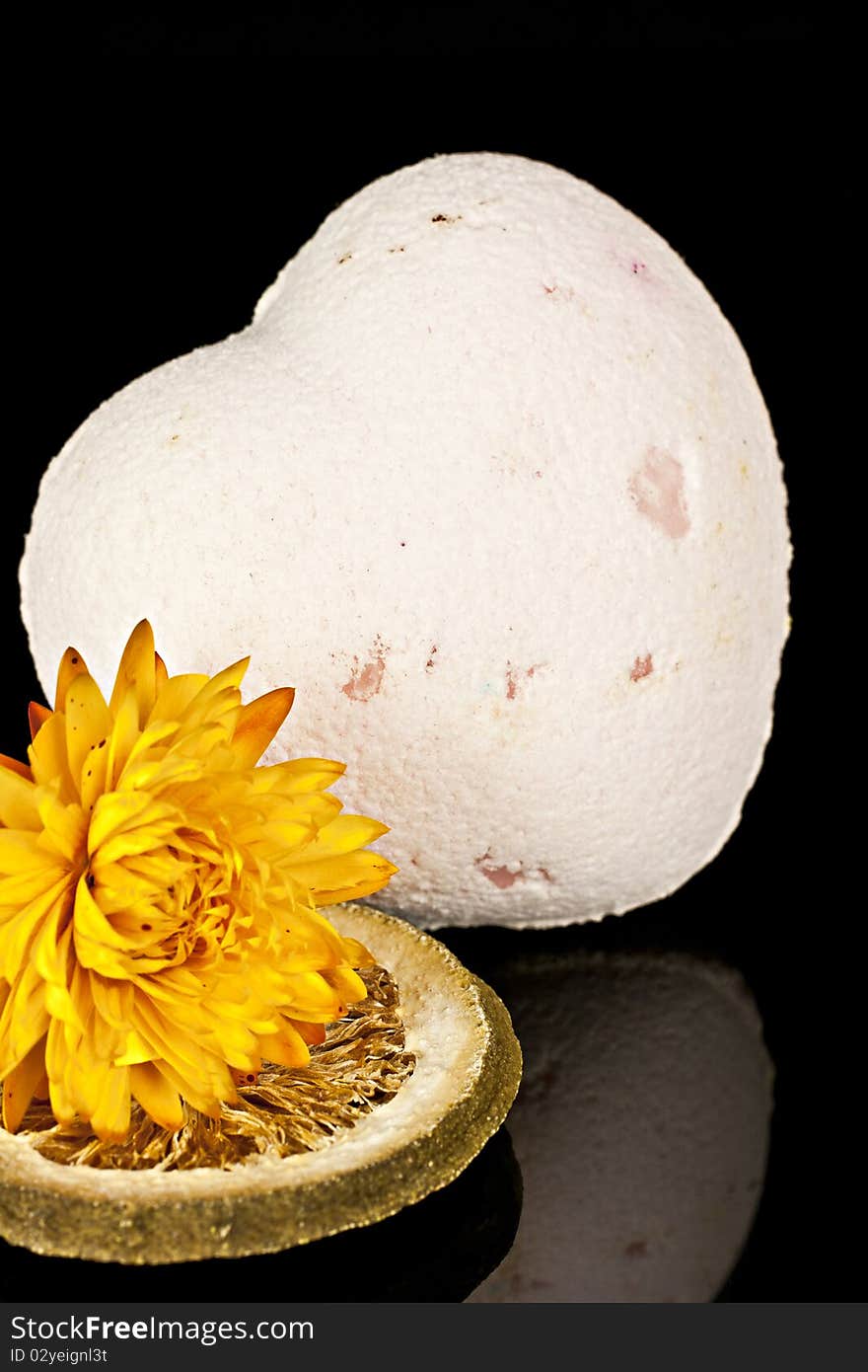 Bath salts in the form of the heart with a dry yellow flowers and the dried slices of lemon on a black background. Bath salts in the form of the heart with a dry yellow flowers and the dried slices of lemon on a black background.