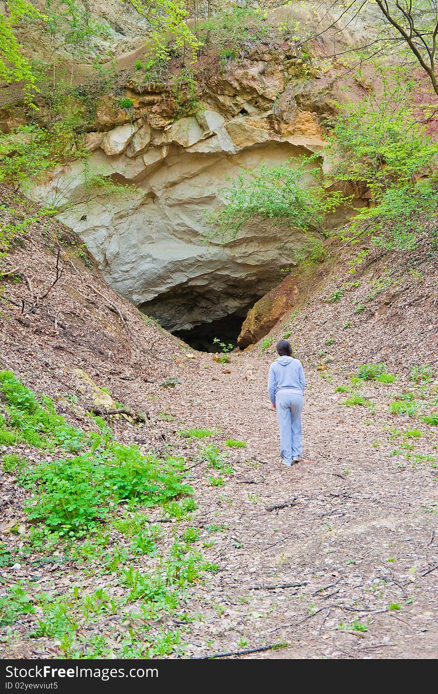 Young woman approaching the entrance of an mountain cave, having doubts about entering or not. Young woman approaching the entrance of an mountain cave, having doubts about entering or not