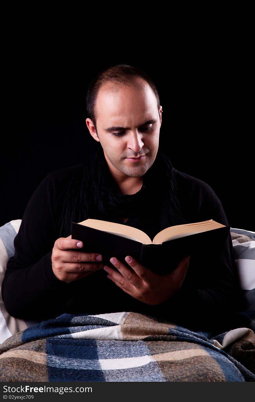 Man lying on the couch reading a book, isolated on black, studio shot.