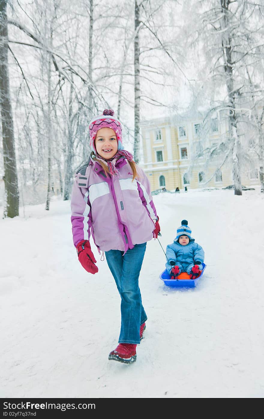 Older sister pulls her brother on a sled in winter park. Older sister pulls her brother on a sled in winter park