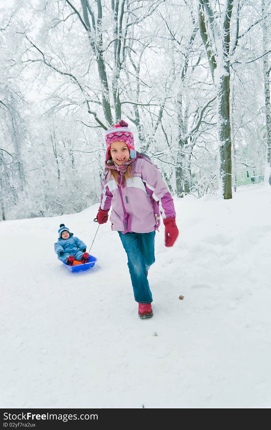 Older sister rolls her brother on a sled in winter park. Older sister rolls her brother on a sled in winter park