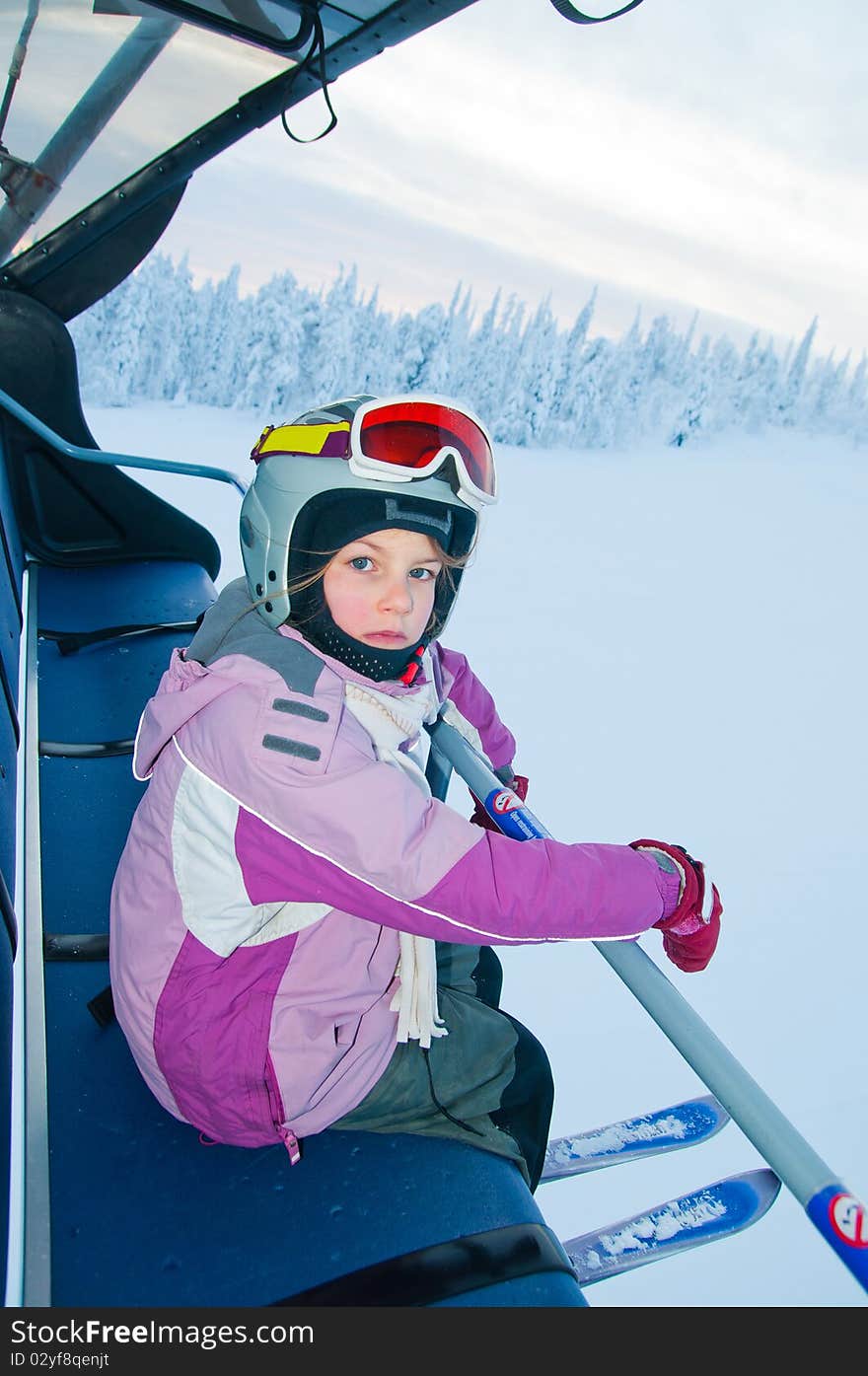 Little girl-skier on the ski lift watching the sunrise at a ski resort in Finland