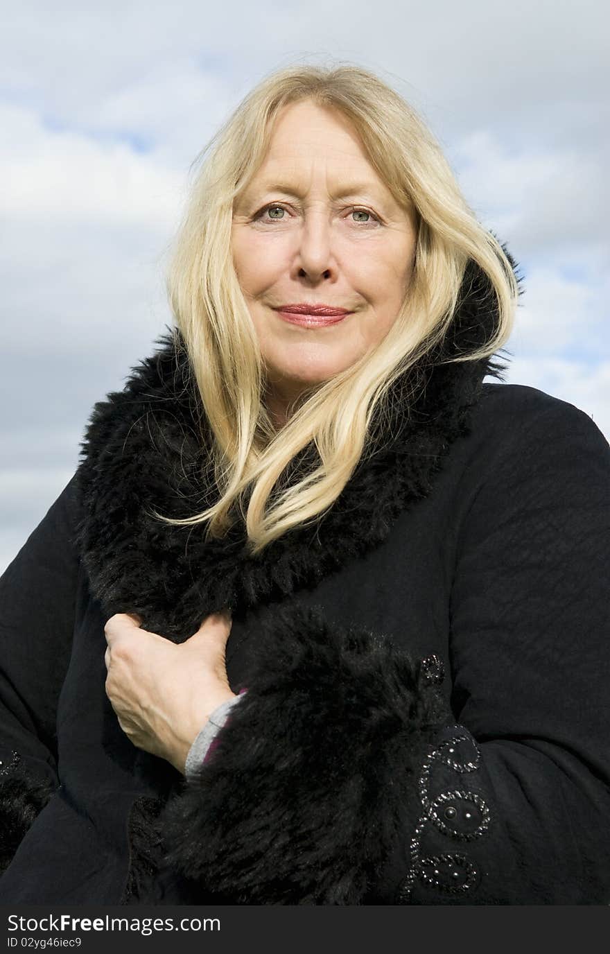 Color portrait photo of a beautiful blonde older lady in her sixties wearing a black winter coat and looking straight at camera. Color portrait photo of a beautiful blonde older lady in her sixties wearing a black winter coat and looking straight at camera.