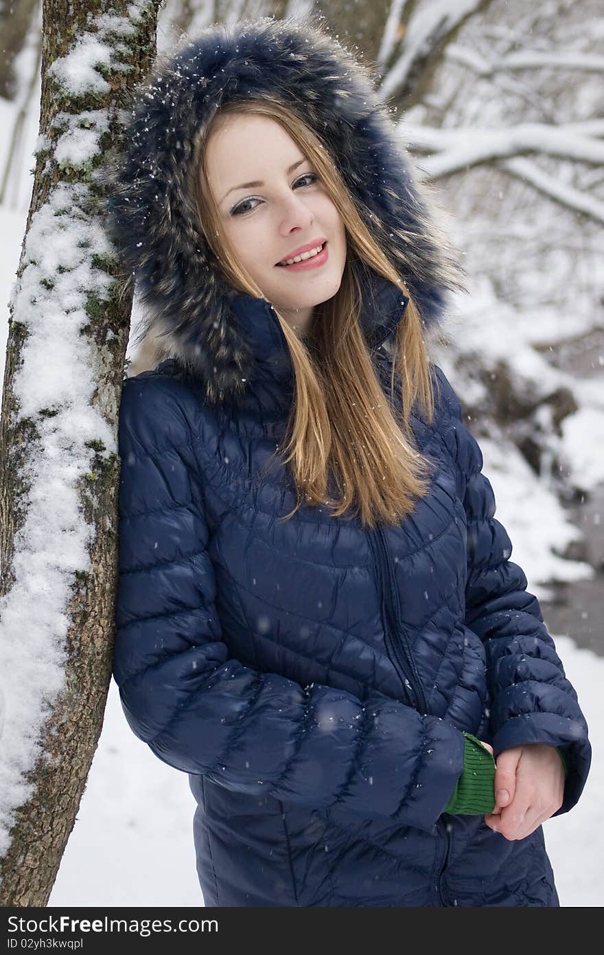 Smiling young woman in blue coat outdoors in snow garden. Smiling young woman in blue coat outdoors in snow garden