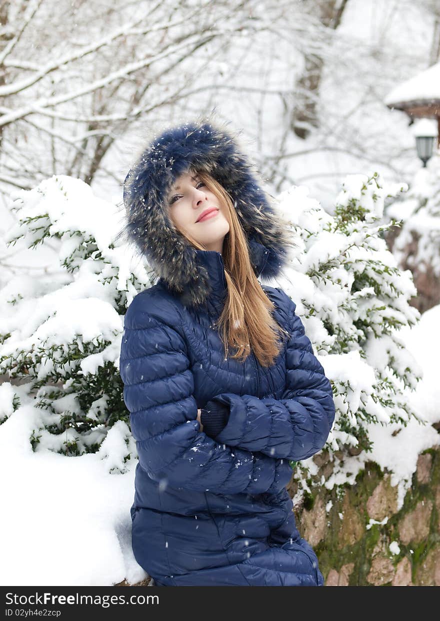 Smiling young woman in blue coat outdoors in snow garden. Smiling young woman in blue coat outdoors in snow garden