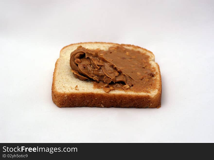 A piece of white bread with peanut butter being spread over it. A piece of white bread with peanut butter being spread over it.