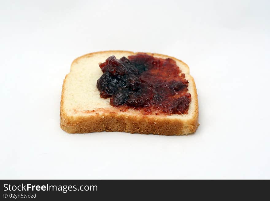 A piece of white bread with strawberry jelly being spread over it. A piece of white bread with strawberry jelly being spread over it.