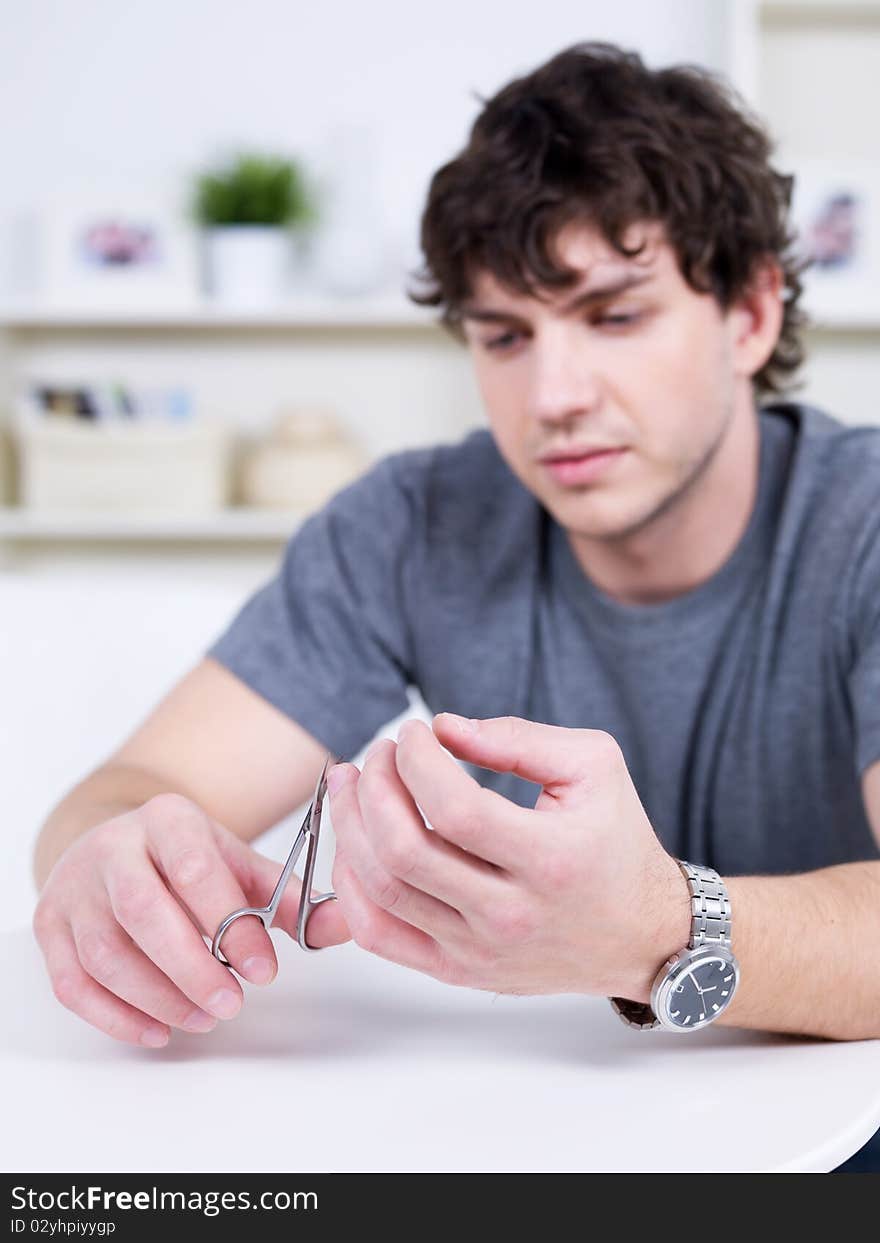 Portrait of handsome young candid man cutting nails - indoors. Portrait of handsome young candid man cutting nails - indoors