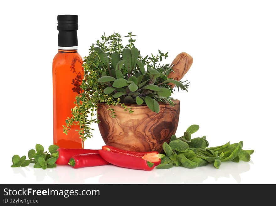 Chilli olive oil, chillies, and herb leaf sprigs of rosemary,  sage, thyme and oregano in an olive wood mortar with pestle, isolated over white background. Chilli olive oil, chillies, and herb leaf sprigs of rosemary,  sage, thyme and oregano in an olive wood mortar with pestle, isolated over white background.
