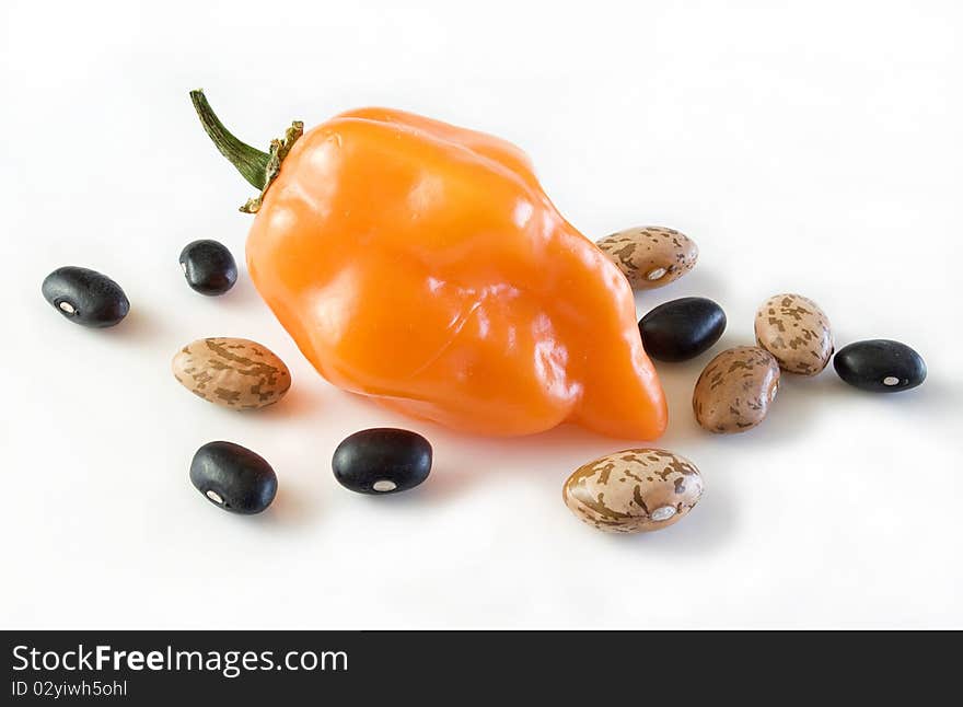 Beautiful ripe golden orange habanero chile surrounded with pinto and black beans, on white. Beautiful ripe golden orange habanero chile surrounded with pinto and black beans, on white.