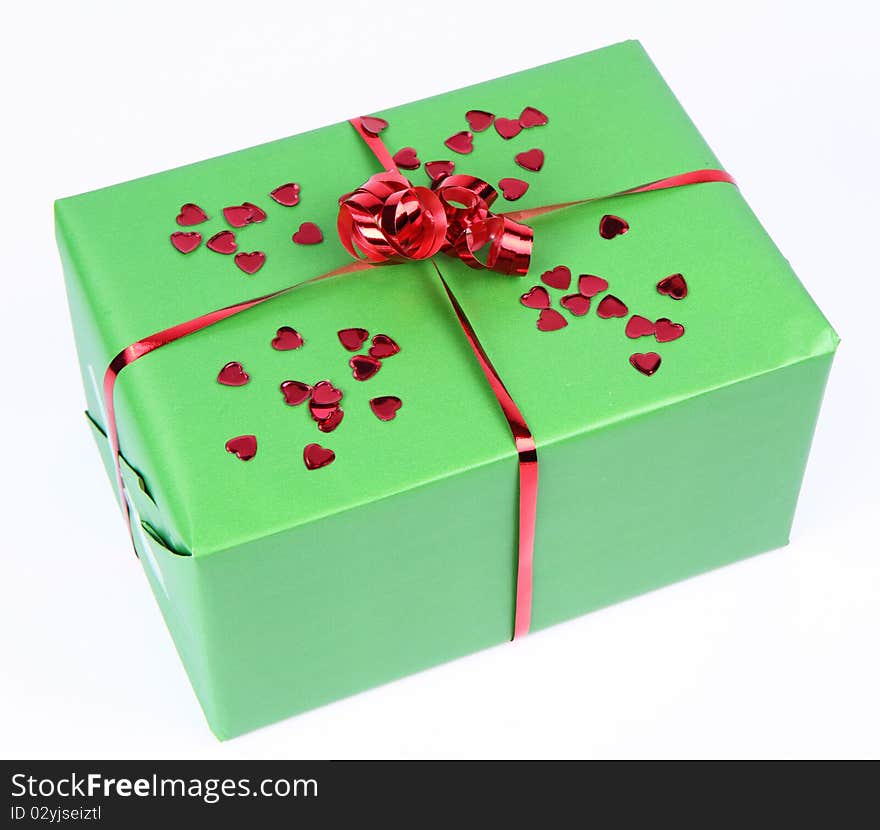 Gift in green wrapping with a red bow decorated with heart shaped confetti. Gift in green wrapping with a red bow decorated with heart shaped confetti