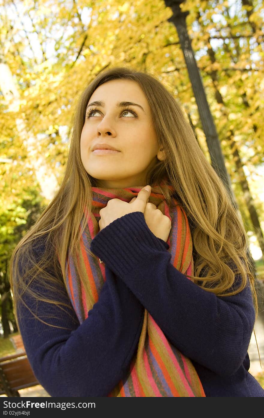 Autumn portrait of a beautiful young woman against yellow leaves. The girl was wrapped in a scarf