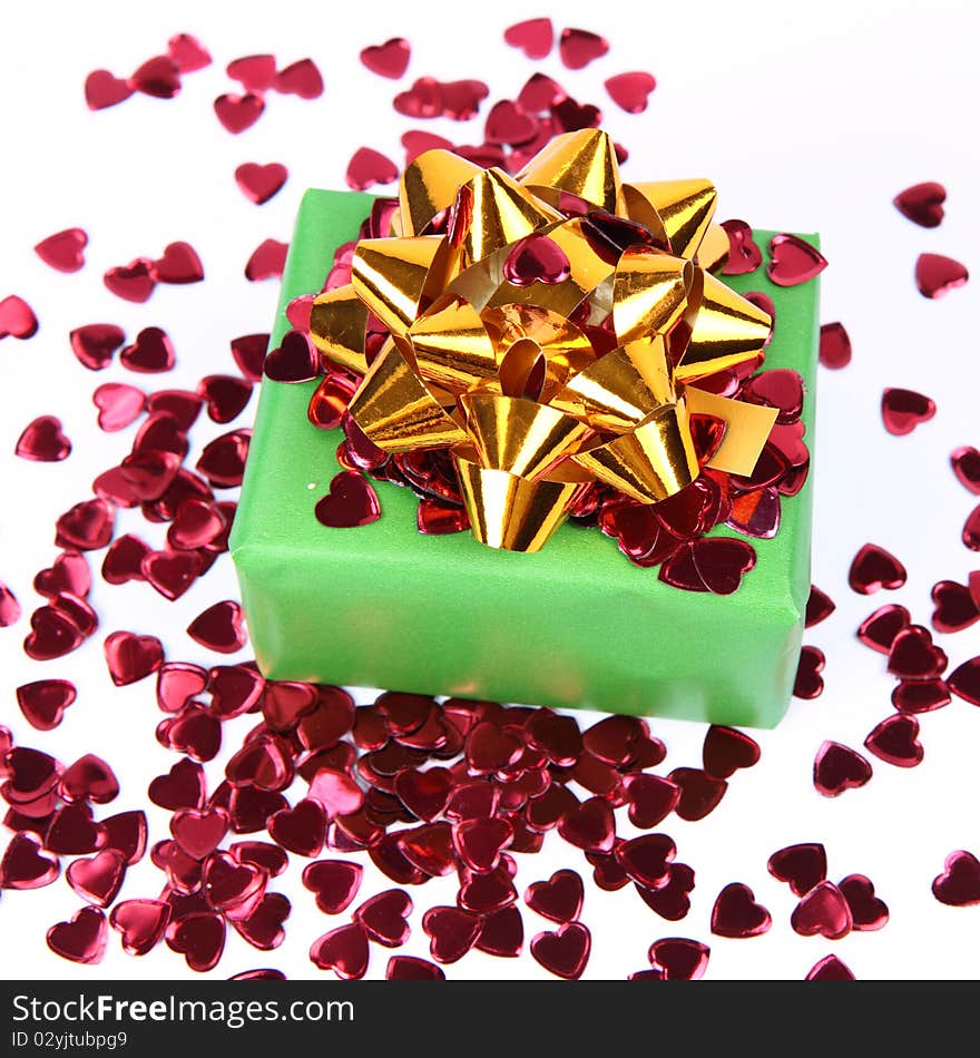 Gift in green wrapping with a golden bow decorated with heart shaped confetti. Gift in green wrapping with a golden bow decorated with heart shaped confetti