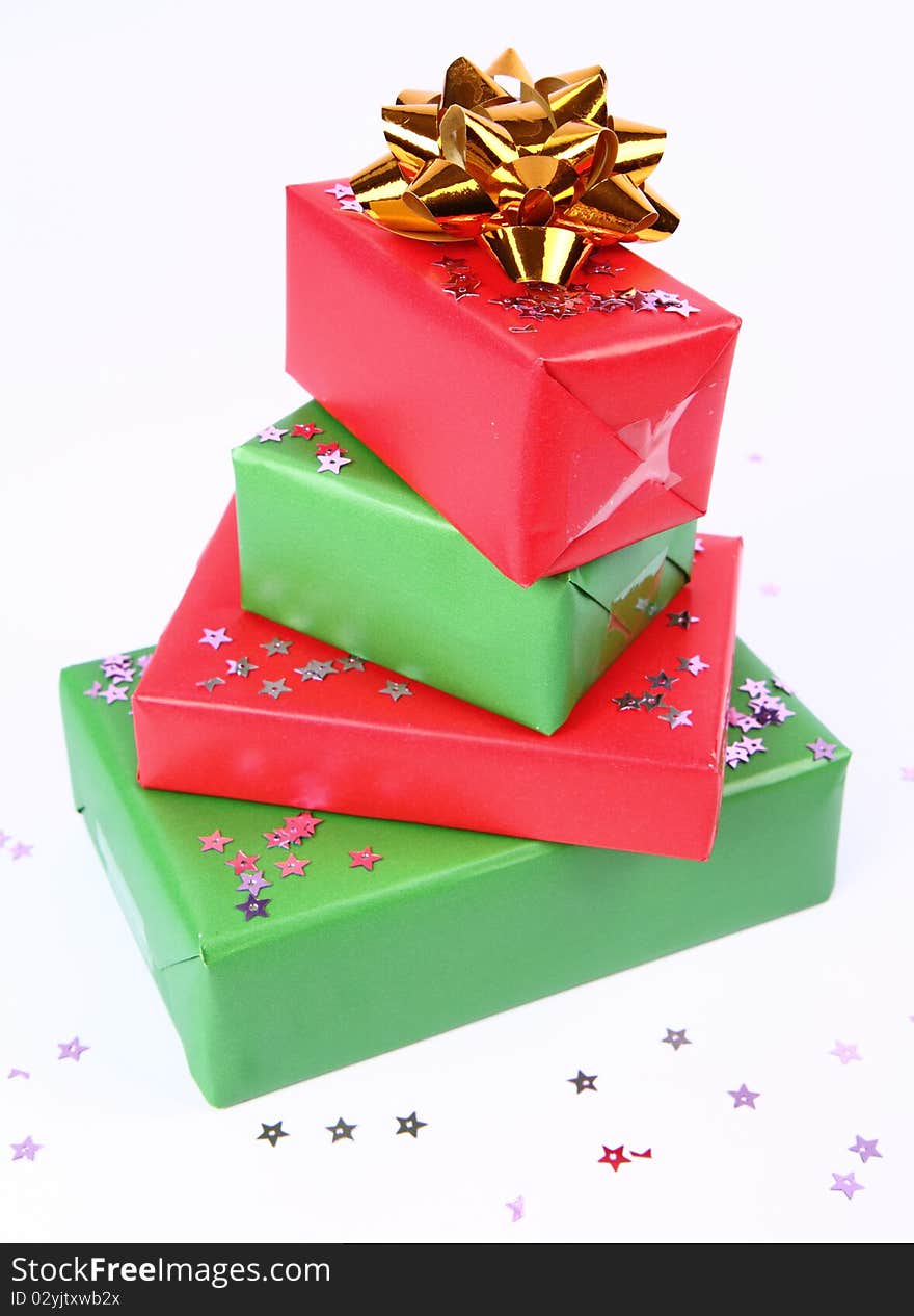 Pile of gifts in green and red wrapping with a golden bow decorated with star shaped confetti