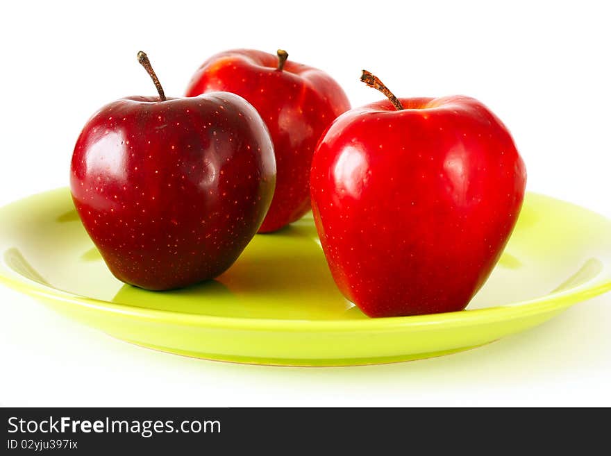 Three Red apples on green plate, white background.